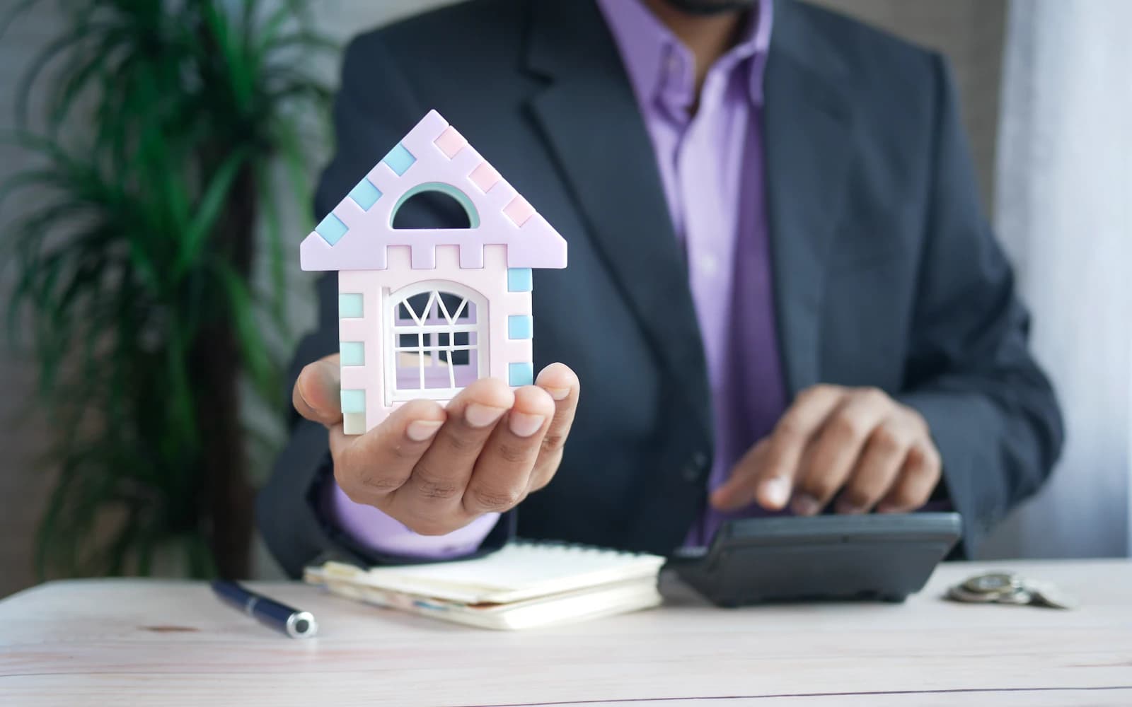 Property professional using a calculator beside a model house